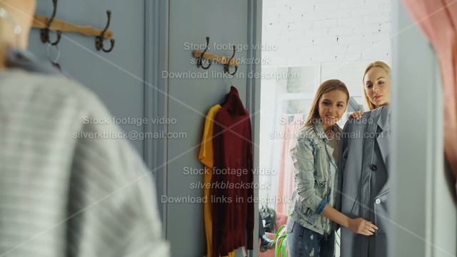 Cheerful young lady is trying coat in fitting room and asking her friend for advice. Girlfriend is смотреть онлайн