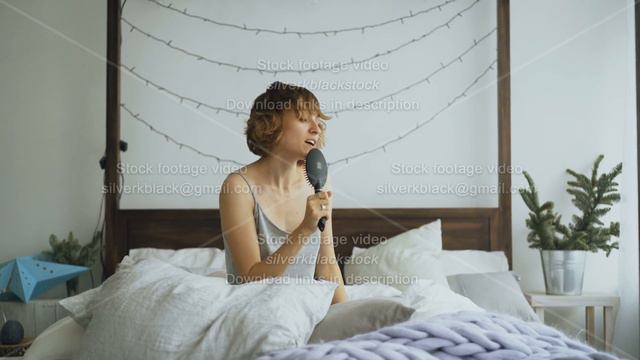 Attractive cheerful woman dancing and singing with comb like microphone sitting in bed at home смотреть онлайн