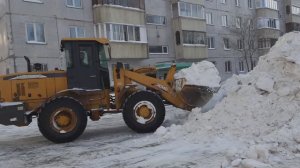 Трактор и самосвал убирают снег во дворе
