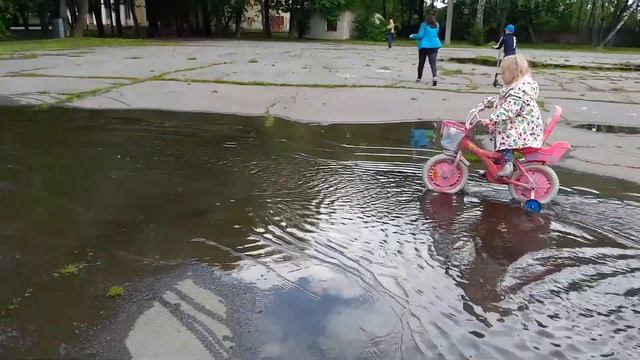 София и Давид на велосипедах катаются по лужам в городском парке. смотреть онлайн