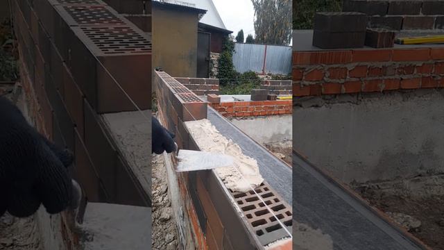 Каменщик кладет ряд керамического кирпича.
