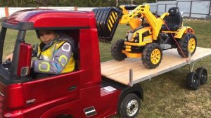 Малыш катается на игрушечной фуре с прицепом и перевозит трактор