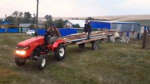 Русич-т18 в работе. Минитрактор перевозит длинные доски на самодельном прицепе.