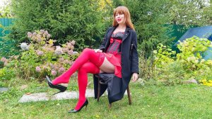 Рыжая девушка в черном пальто и в красных чулках демонстрирует черно-красный стиль и танцует