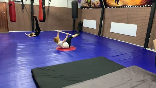 Дети тренируются падать перекатом назад с прямыми ногами с палкой смотреть онлайн