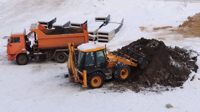 Зимой экскаватор-погрузчик загружает самосвал. смотреть онлайн